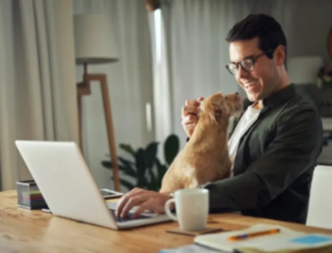 Man sitting with a brown dog while using his laptop at home